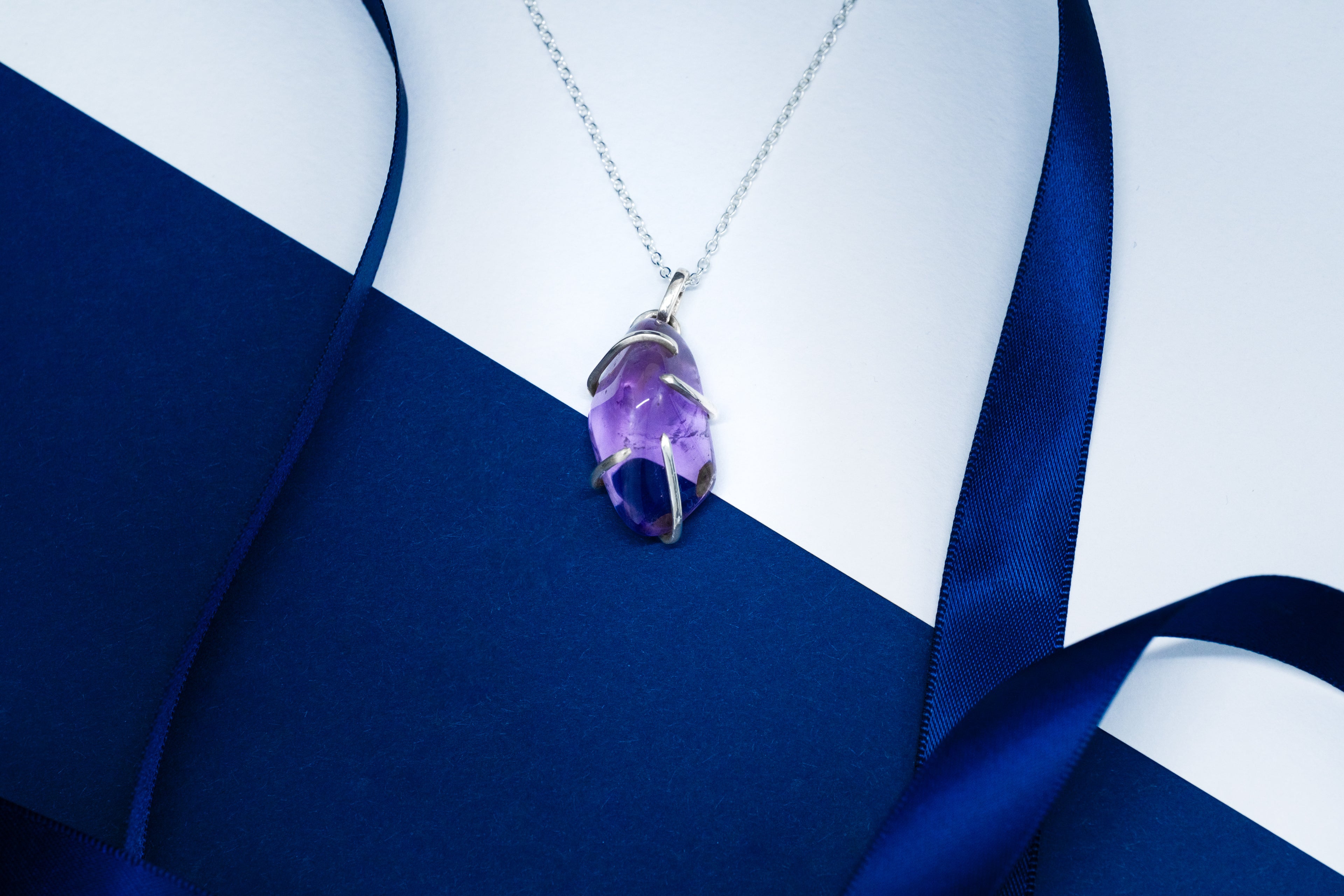 Necklace with a purple pendant on a blue and white fabric background