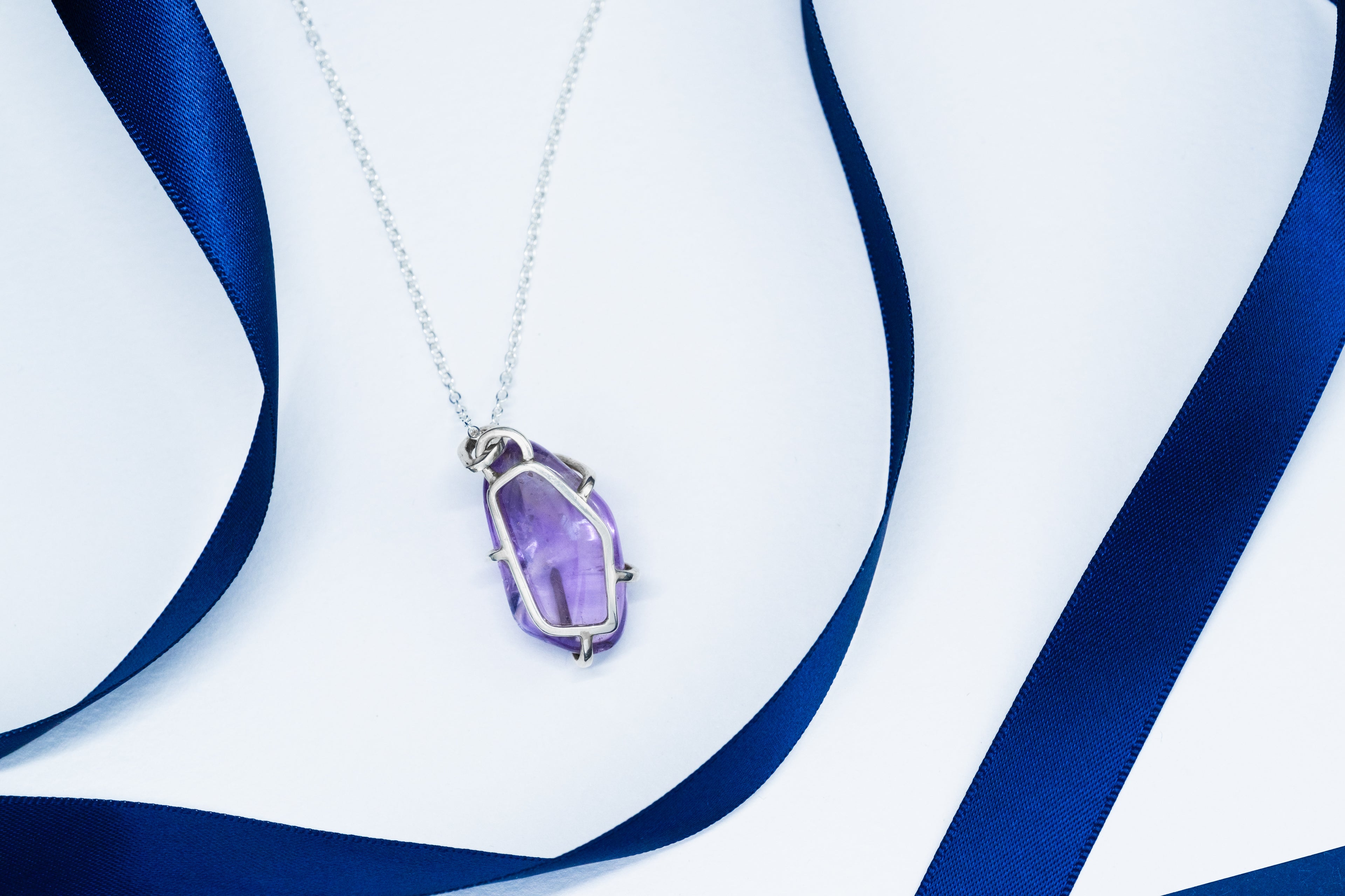 Purple pendant necklace on a white and blue ribbon background