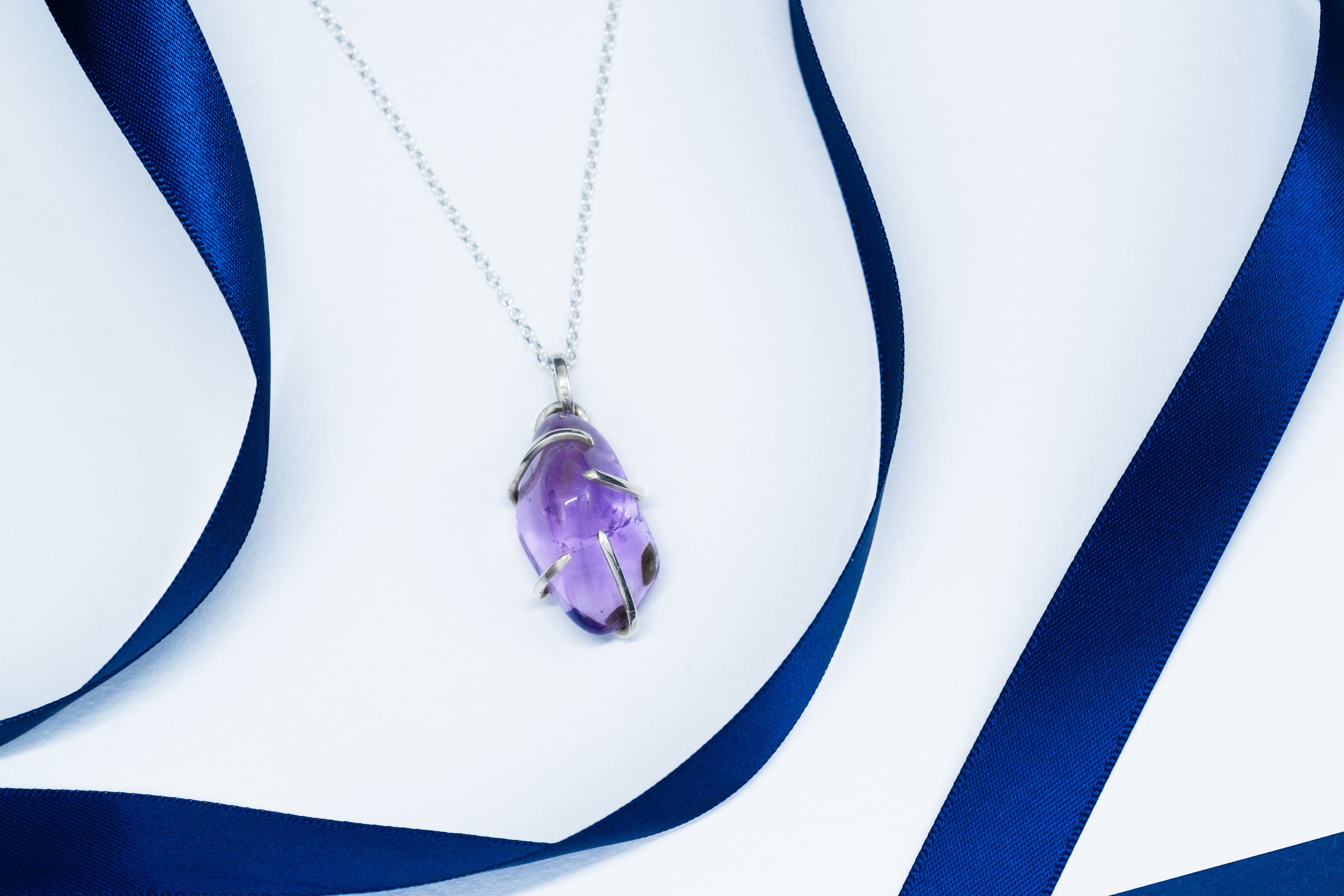 Purple teardrop pendant on a silver chain with blue ribbons in the background