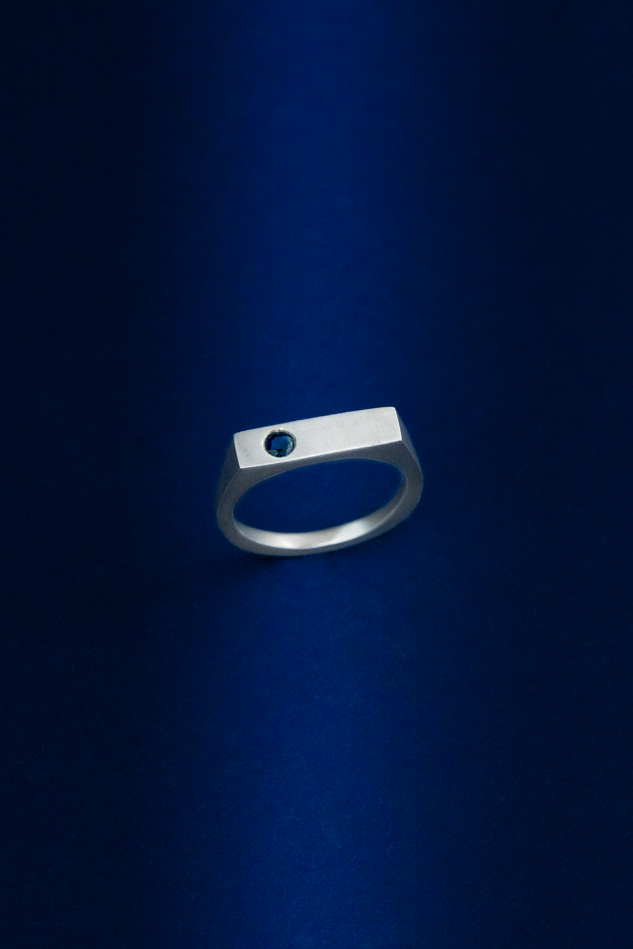 Silver ring on a dark blue background with a blue sapphire gemstone