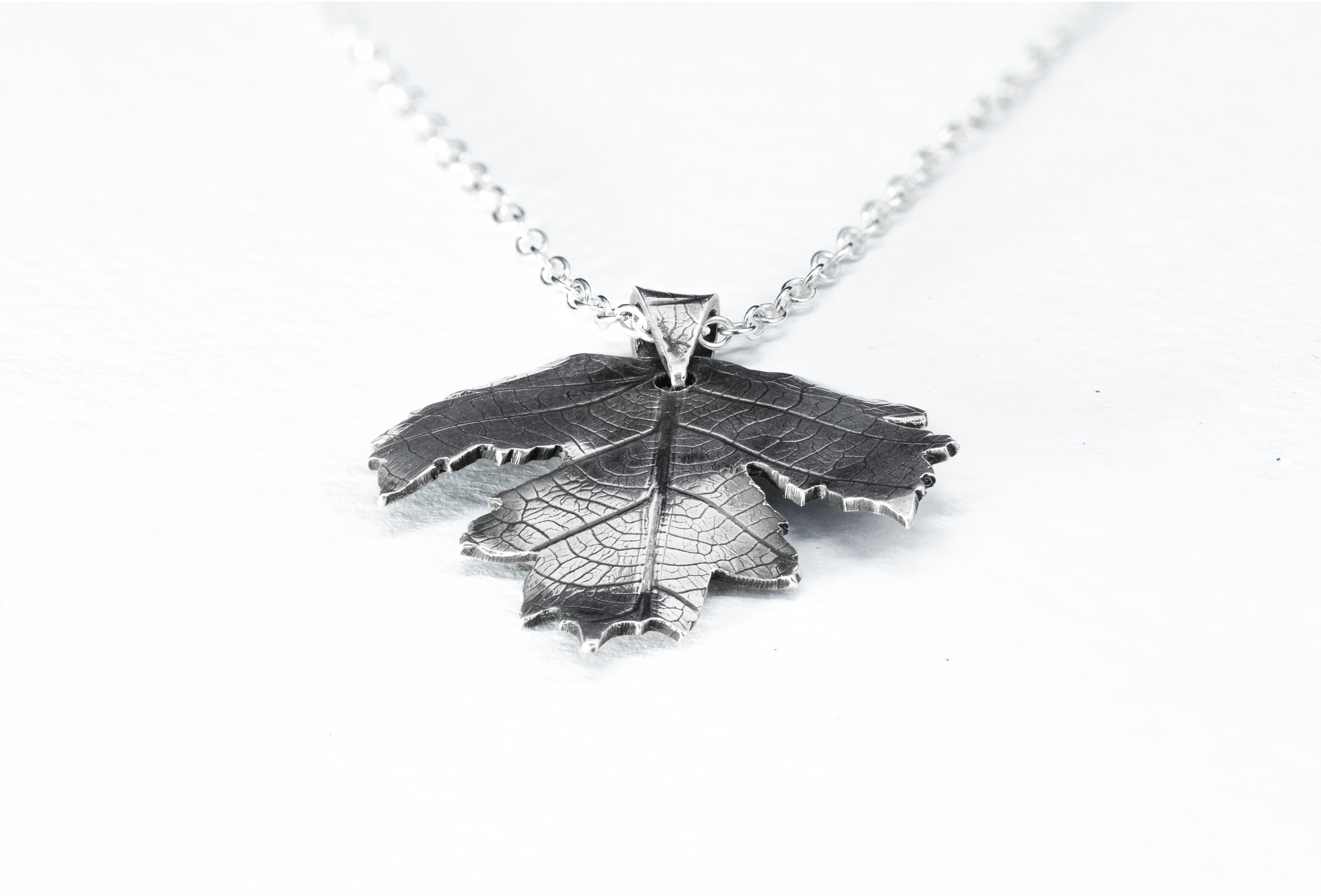 Silver leaf-shaped pendant on a chain against a white background