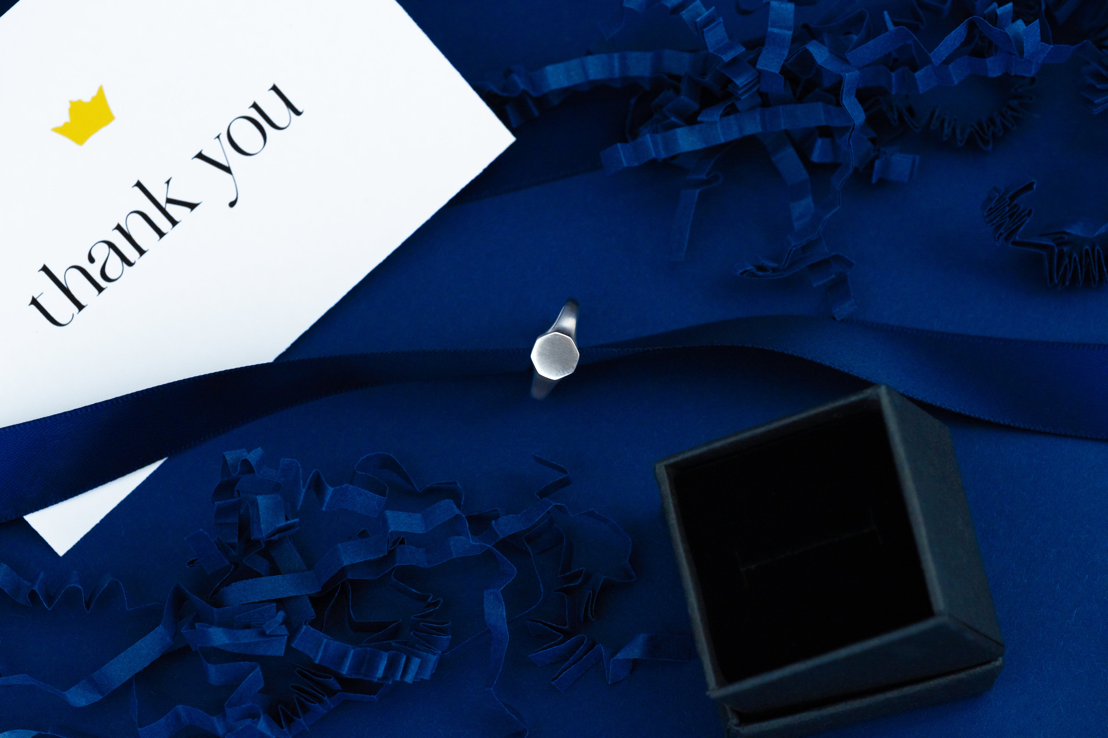 Black jewelry box with a 'thank you' card on a blue fabric background