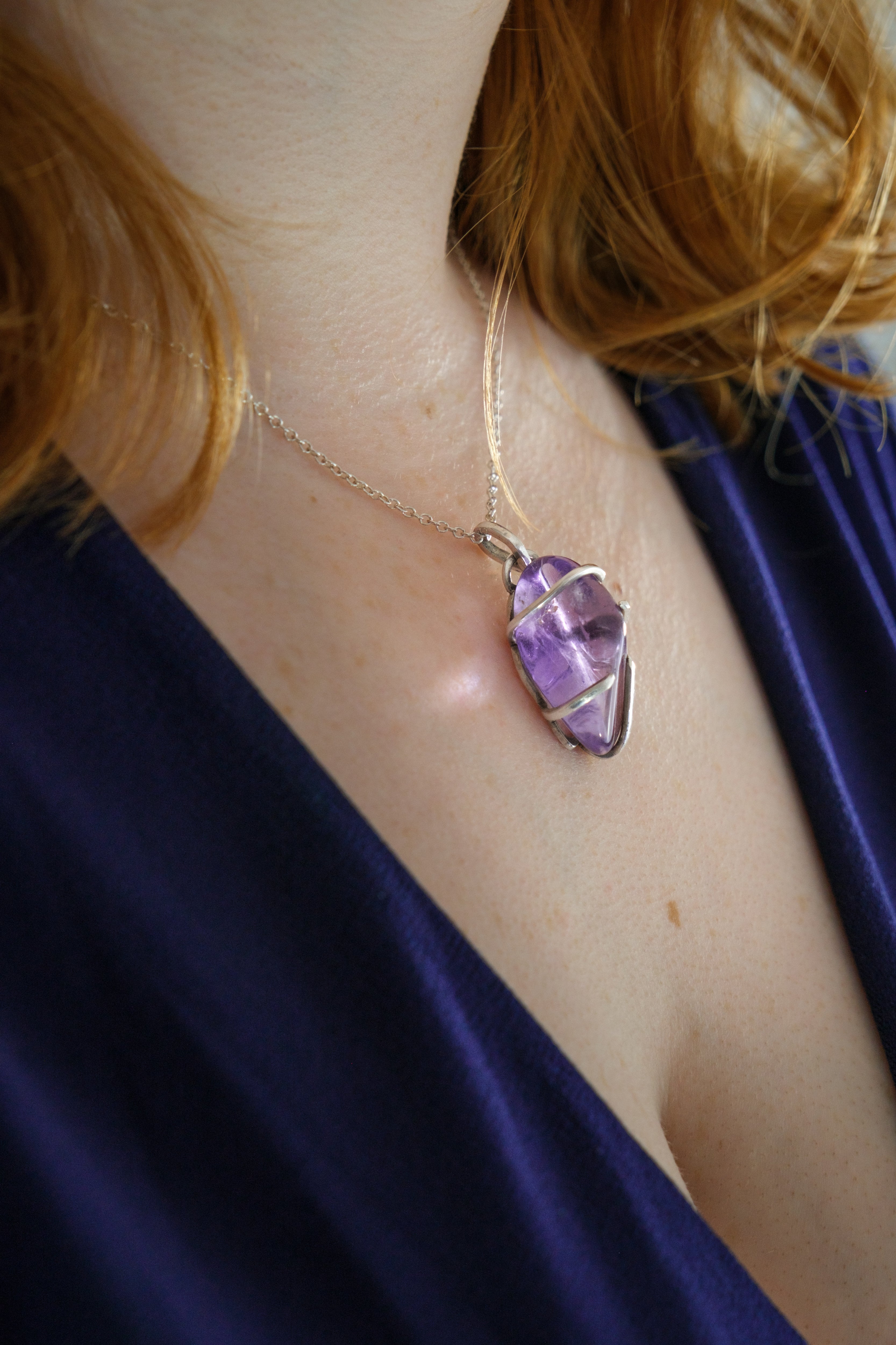 Necklace with a purple gemstone pendant worn by a person against a blue fabric background
