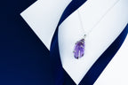 Purple amethyst pendant on a silver chain against a white and blue fabric background