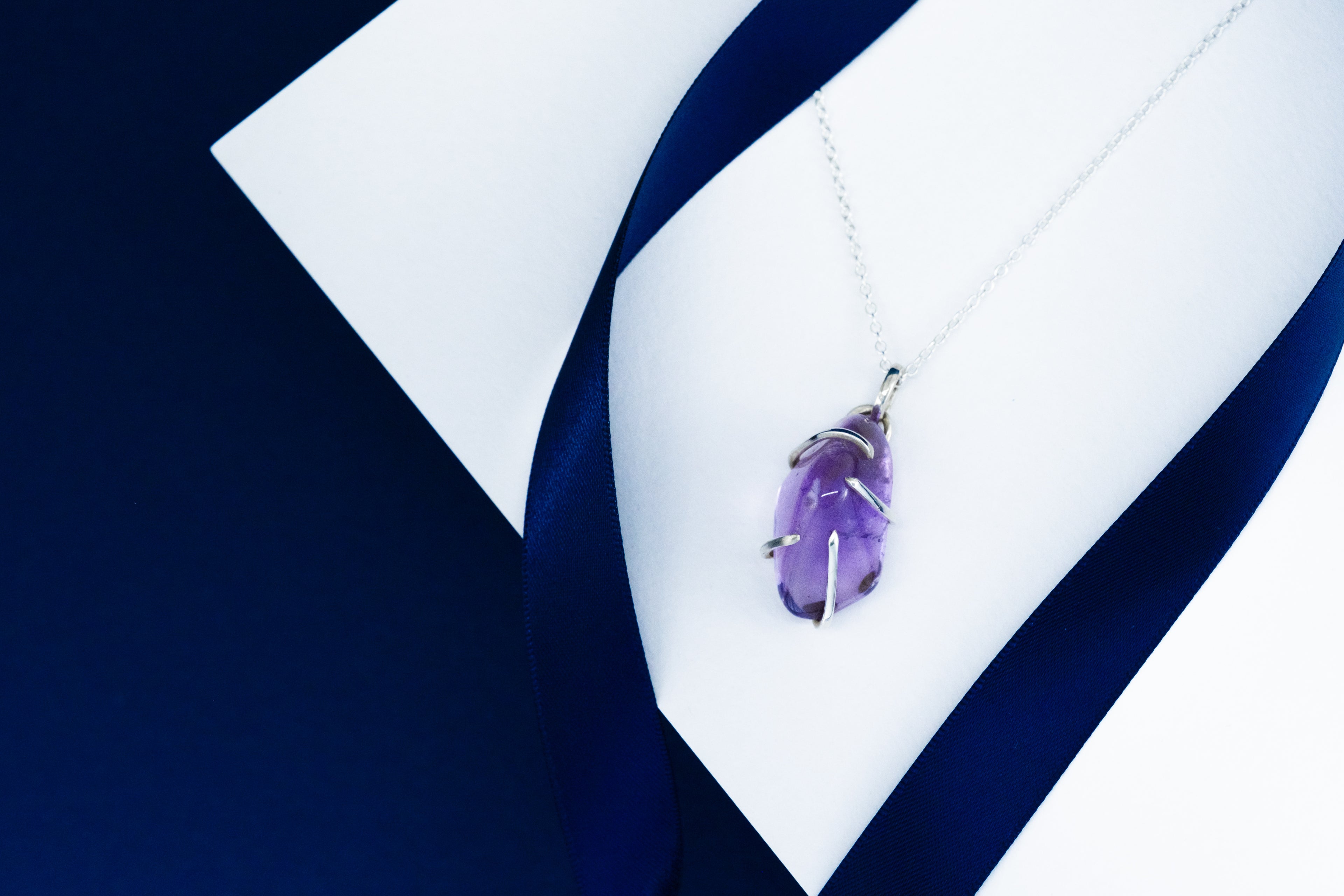 Purple amethyst pendant on a silver chain against a white and blue fabric background