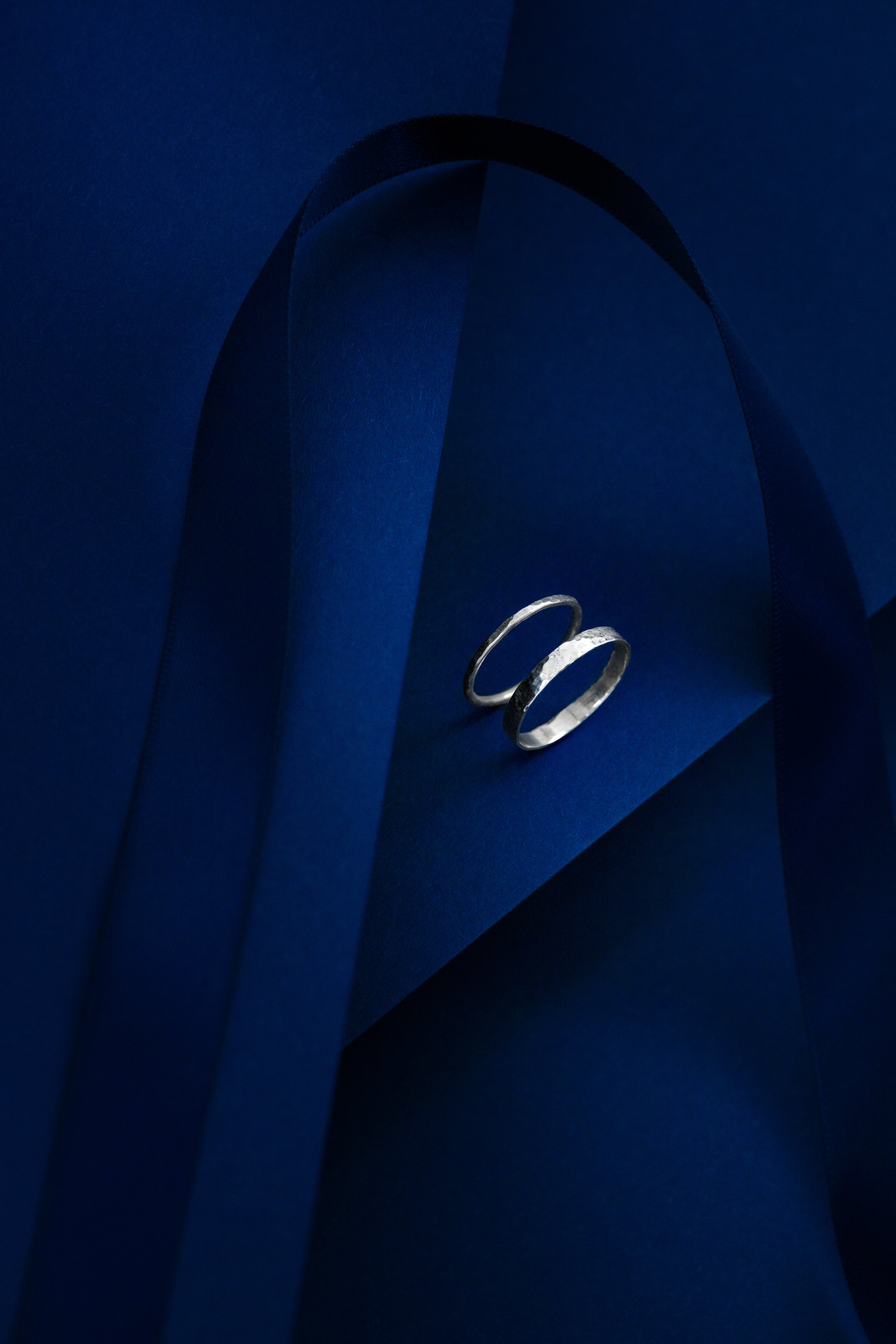 Silver rings on a blue fabric background, one thin, one thicker in width