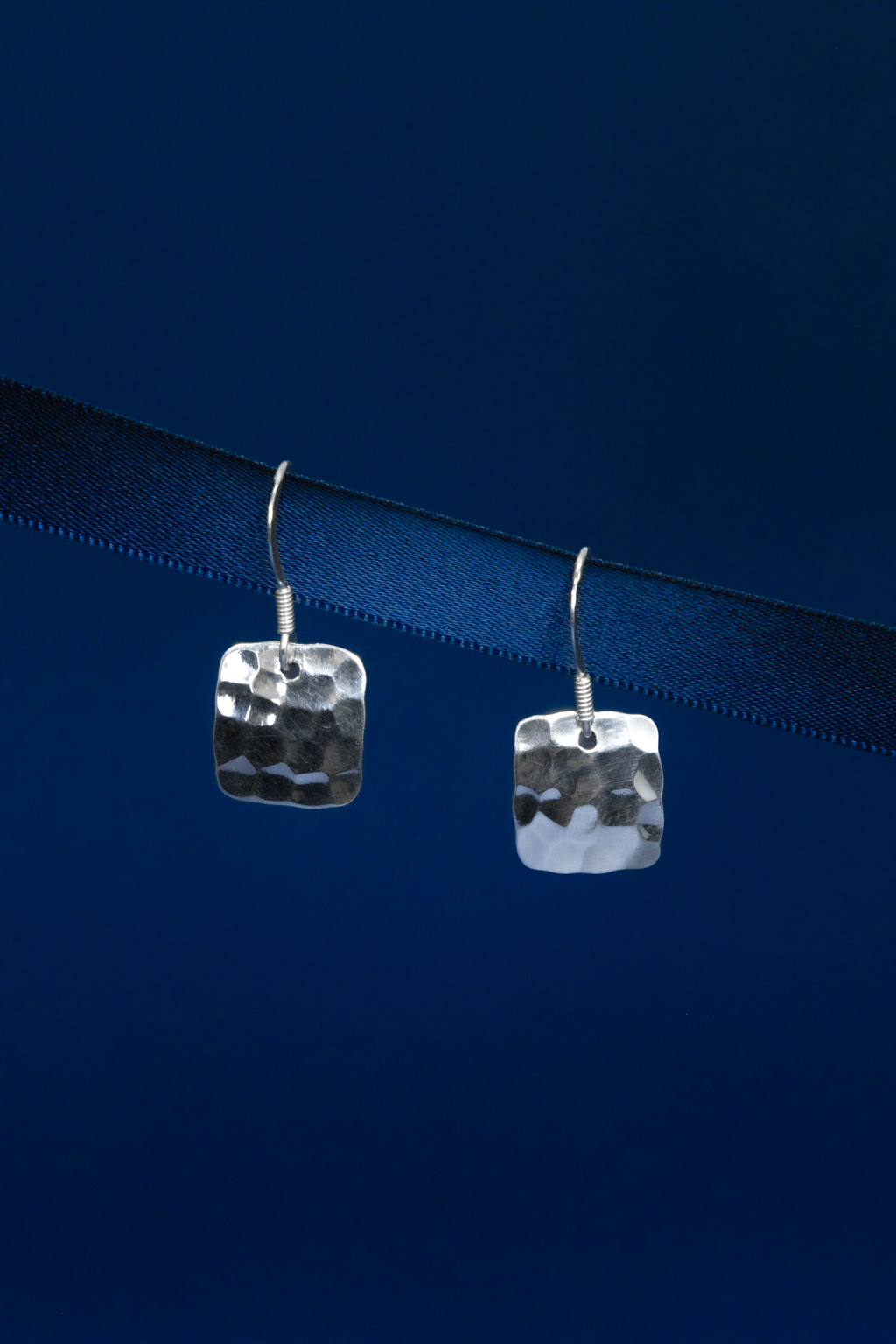 Pair of silver square earrings on a dark blue background