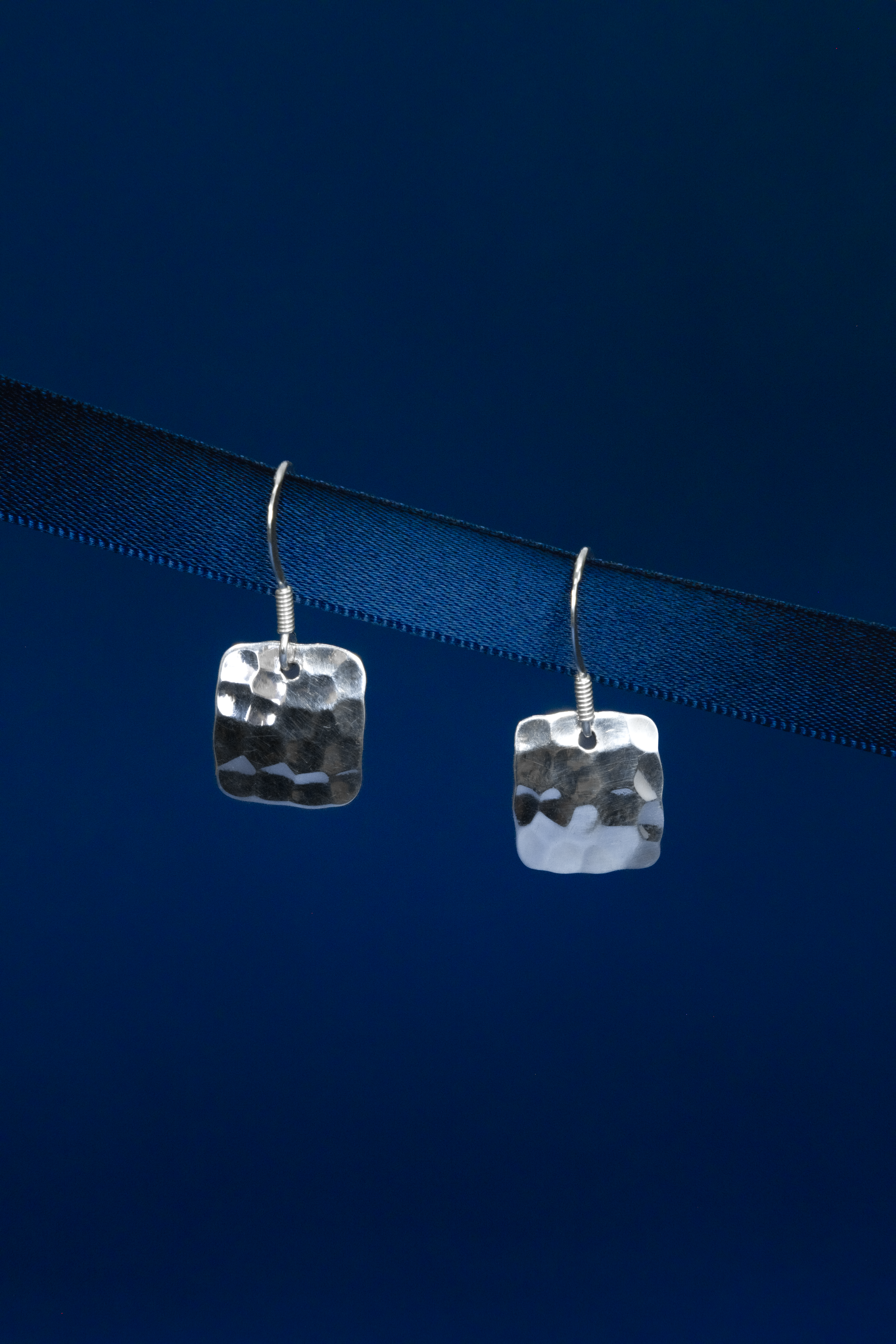 Pair of silver square earrings on a dark blue background