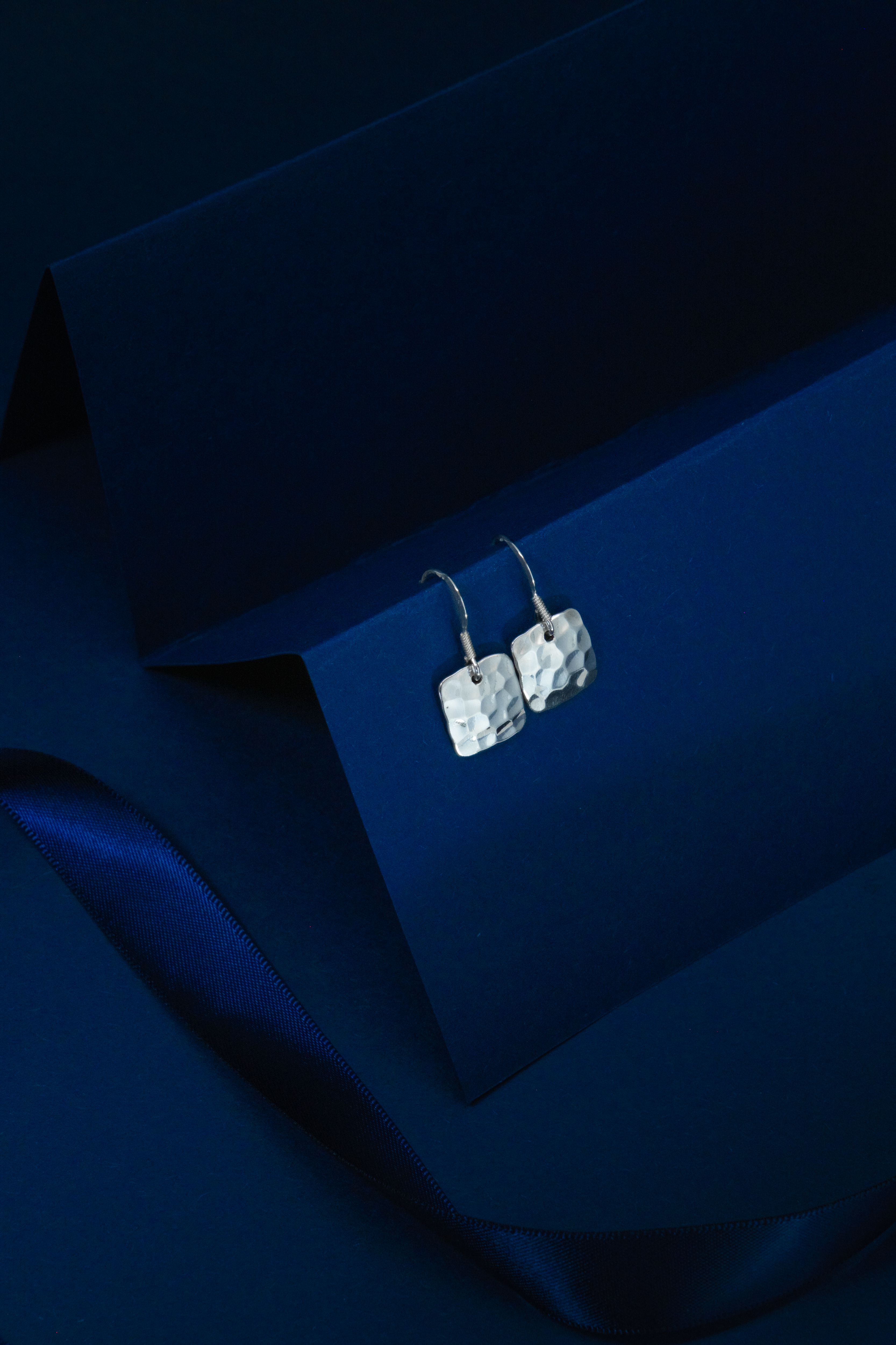 Silver earrings on a dark blue fabric background