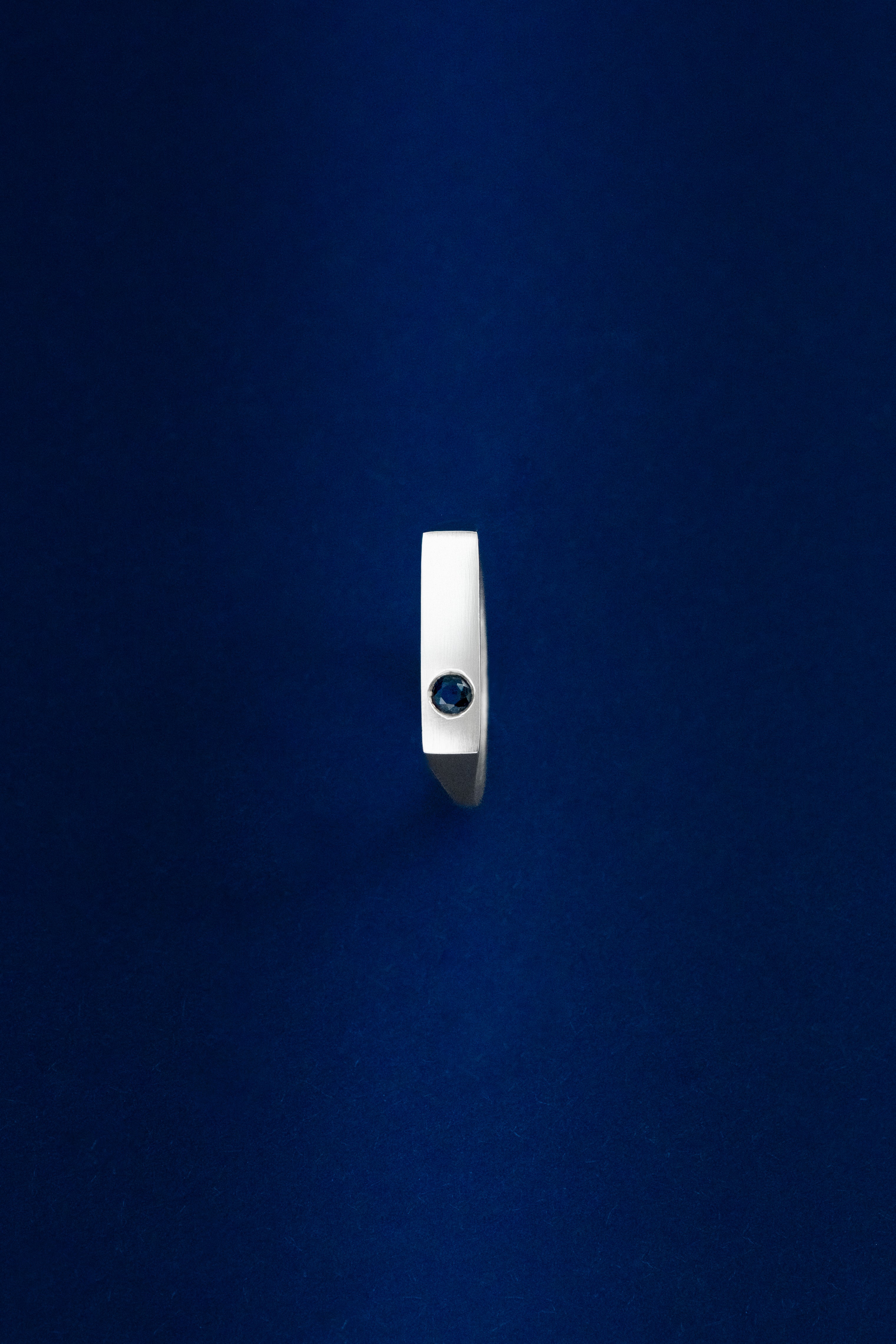 Silver ring with a dark gemstone on a blue background