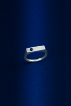 Silver ring on a dark blue background with a blue sapphire gemstone