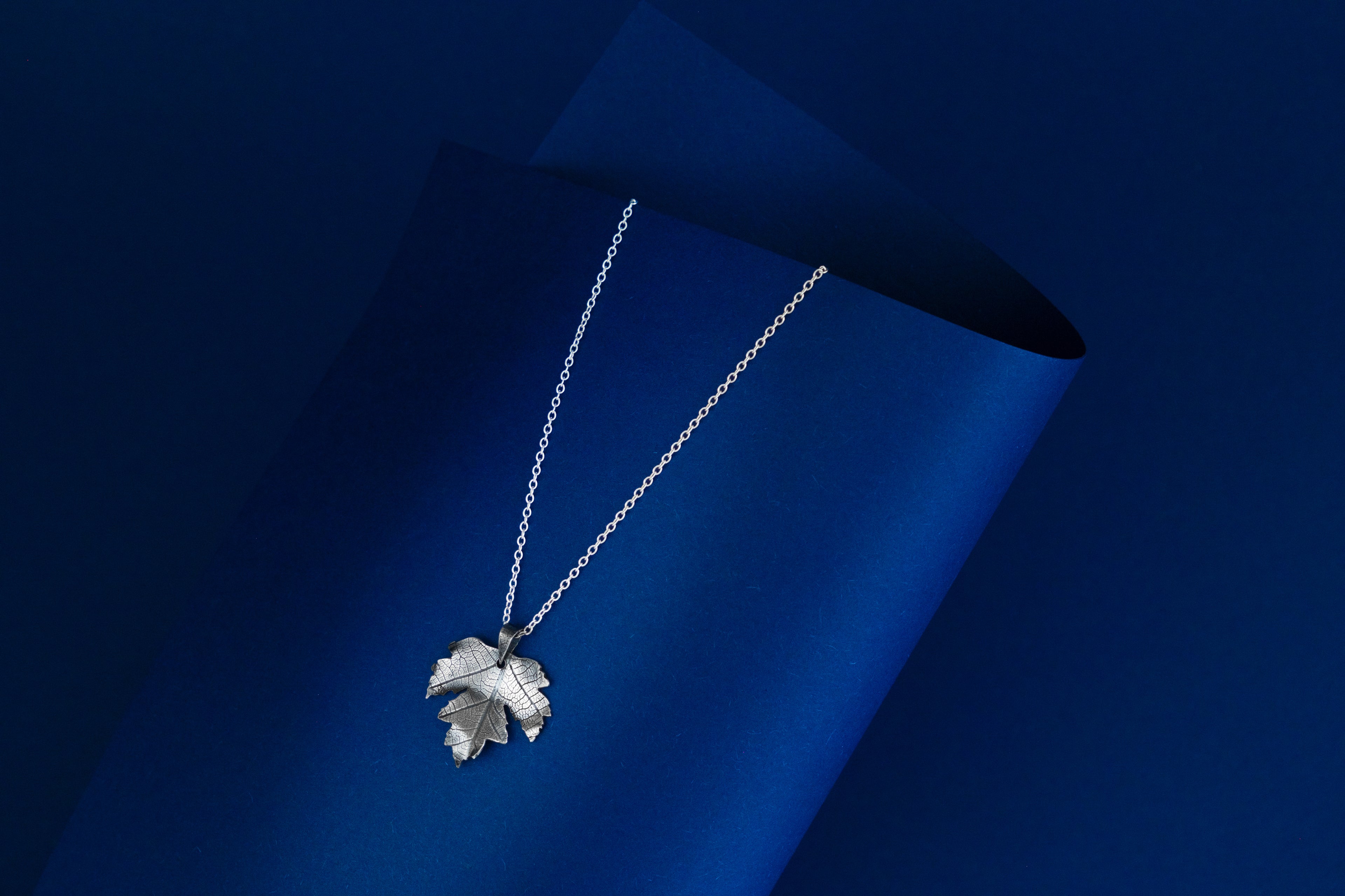 Silver necklace with a leaf pendant on a blue background