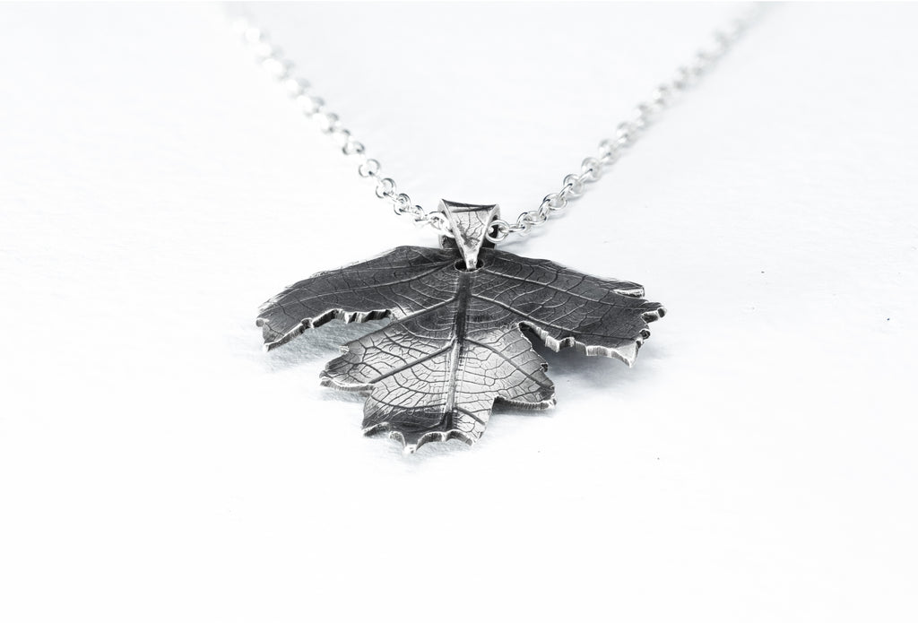 Silver leaf-shaped pendant on a chain against a white background