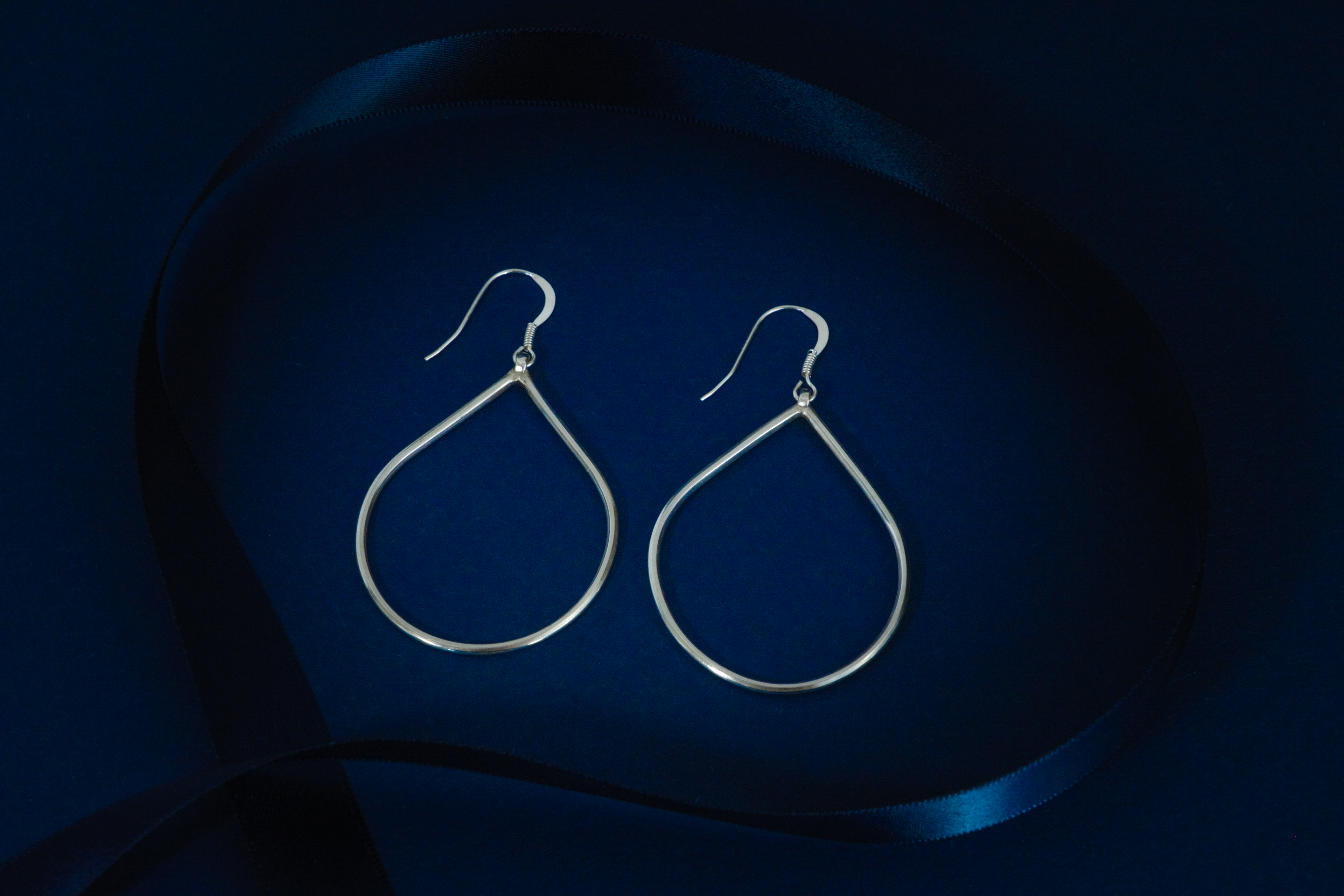 Pair of silver teardrop earrings on a dark blue background